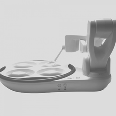 White plastic robotic arm with spoon poised over an attached plate containing four sections. Side view.